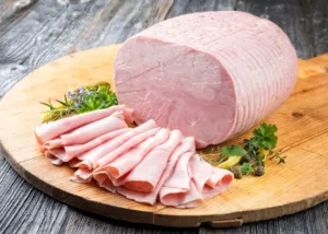 Cooked ham slices on a wooden board, illustrating the use of proteases in meat processing for improved tenderness and protein modification