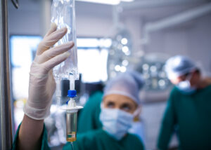 Gloved hand holding an IV drip bag containing yellowish solution in a clinical setting—illustrating Nagase’s Maltose PH, a pharmaceutical-grade excipient for intravenous formulations and patient care applications.