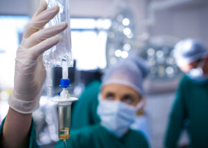 Gloved hand holding an IV drip bag containing yellowish solution in a clinical setting—illustrating Nagase’s Maltose PH, a pharmaceutical-grade excipient for intravenous formulations and patient care applications.
