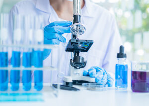 Scientist using a microscope in a modern laboratory with test tubes and reagents—illustrating Nagase’s research reagents for precision bioassays, glycobiology, enzyme analysis, and pharmaceutical development.