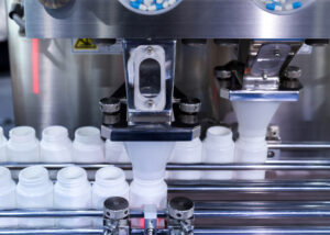 Automated machinery filling white plastic bottles with blue and white capsules, representing Bulk OEM Material by Nagase. The image showcases the precision and efficiency of the pharmaceutical manufacturing process..