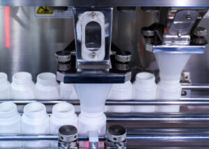 Automated machinery filling white plastic bottles with blue and white capsules, representing Bulk OEM Material by Nagase. The image showcases the precision and efficiency of the pharmaceutical manufacturing process..