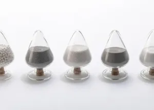 Selection of YTZP grinding media in various grain sizes and forms, displayed in glass sample containers for high-performance milling applications.